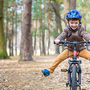 Lachendes Kind trägt einen Fahrradhelm und fährt auf einem Fahrrad durch den Wald.